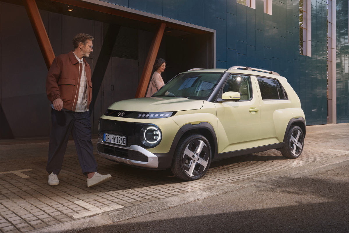 Ein Hyundai Inster steht vor Gebäude. Zwei Personen stehen daneben.