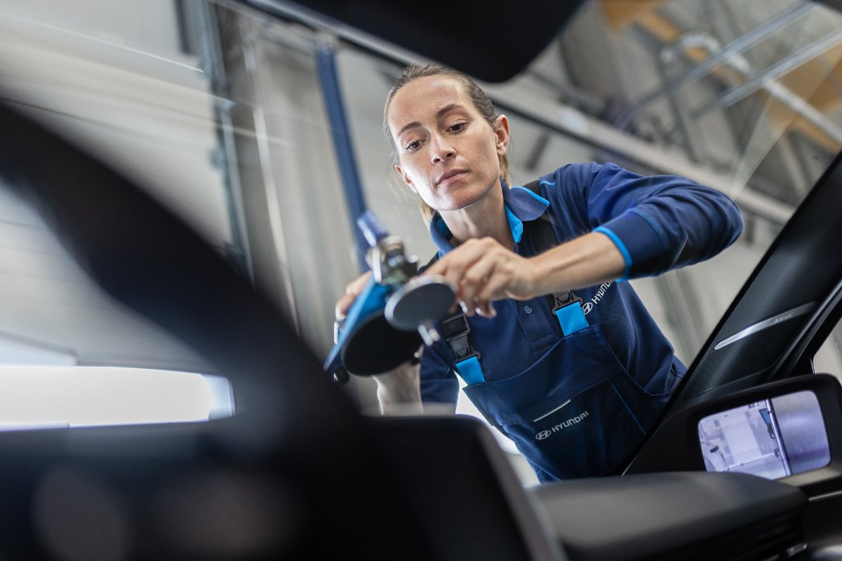 Eine Kfz-Mechanikerin in Hyundai-Arbeitskleidung montiert eine Windschutzscheibe an einem Auto.