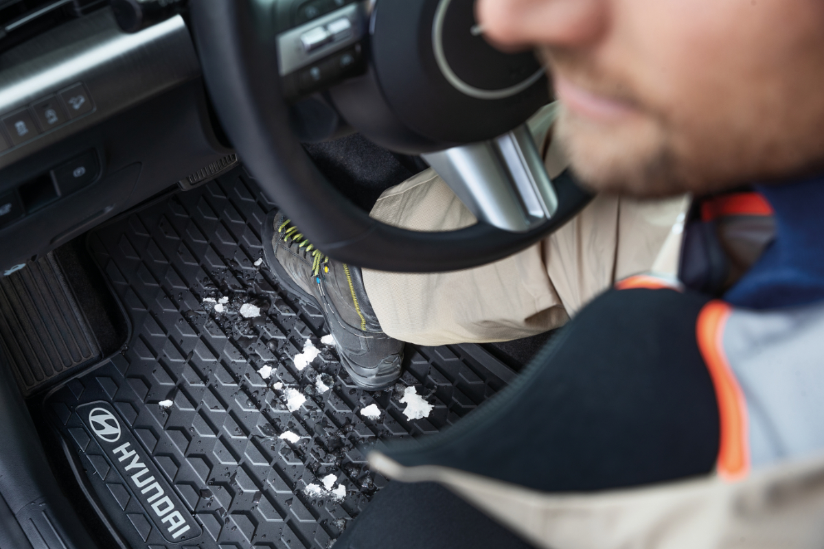 Mann sitzt im Auto, Schneereste auf der Hyundai-Gummimatte unter seinen Schuhen.