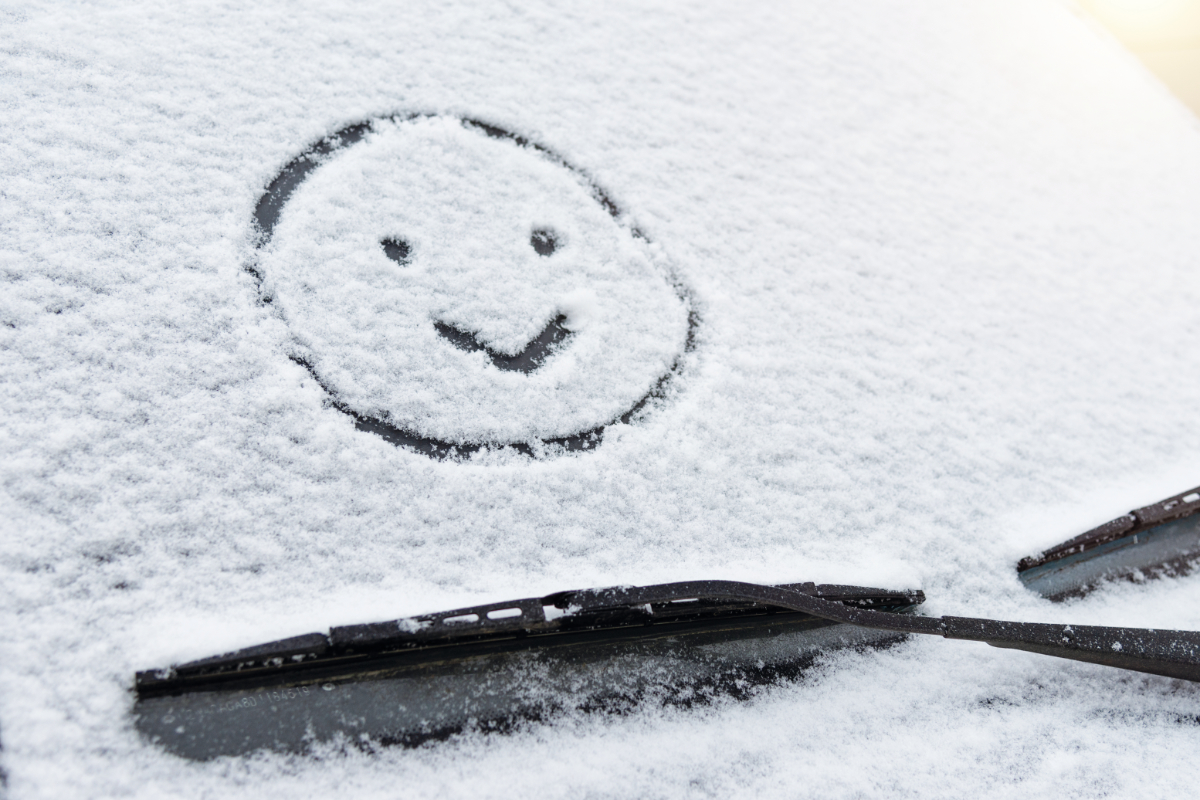 Schneebedeckte Autoscheibe mit einem ins Eis gemalten Smiley und sichtbaren Scheibenwischern.