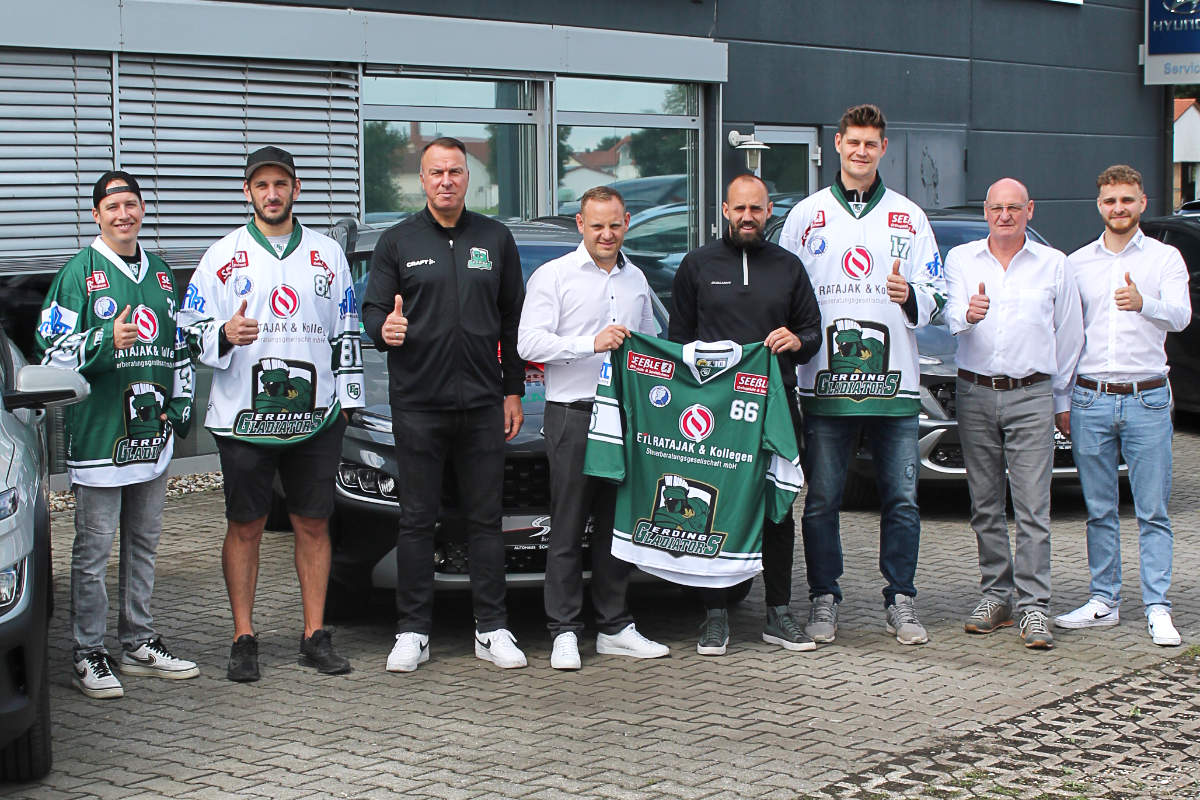 Die Familie Schneider und die Mitglieder der Erding Gladiators stehen vor Autos. Zwei Personen halten Trikots der Erding Gladiators.