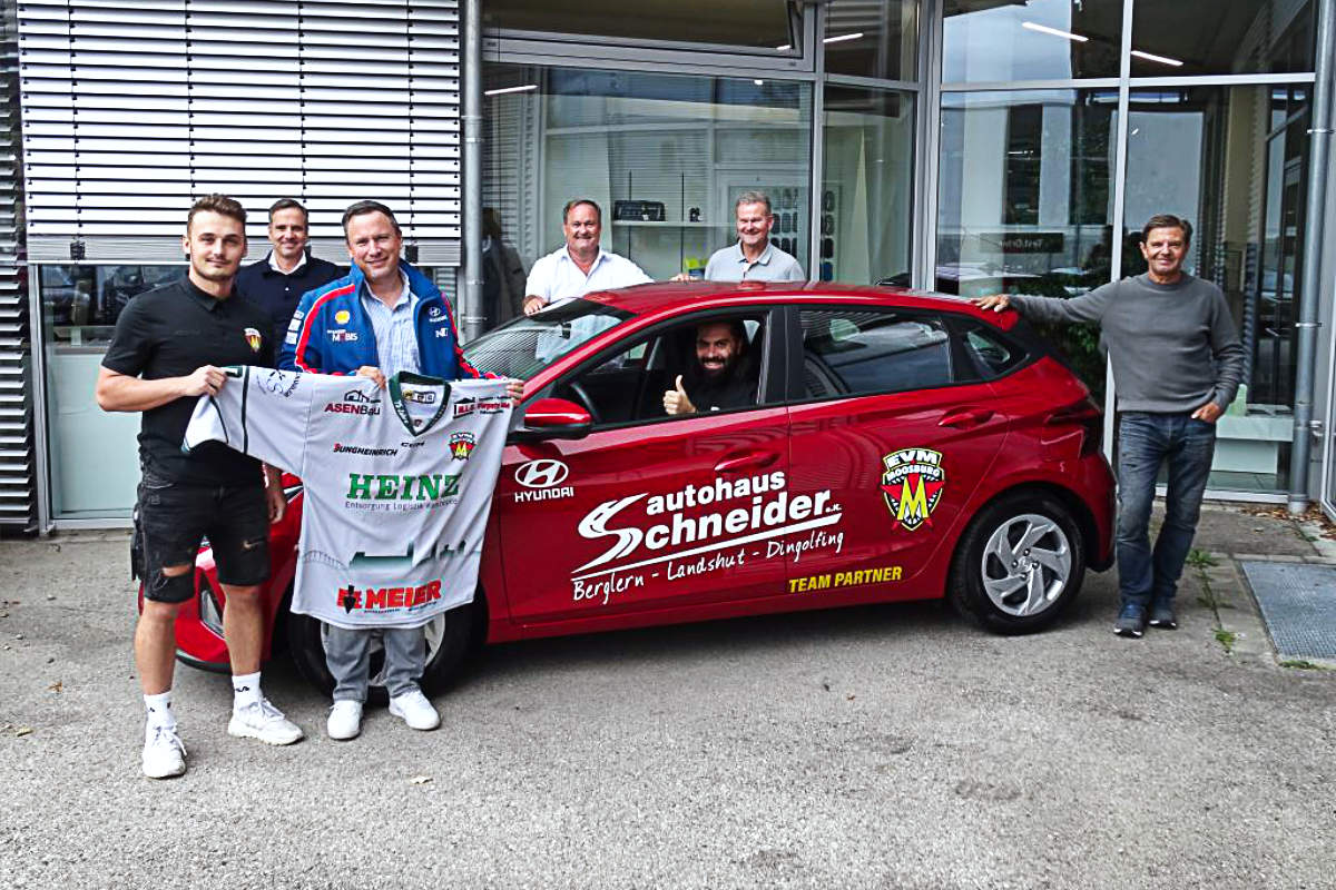 Sechs Männer stehen neben einem Auto, einer sitzt im Auto vor dem Autohaus Schneider