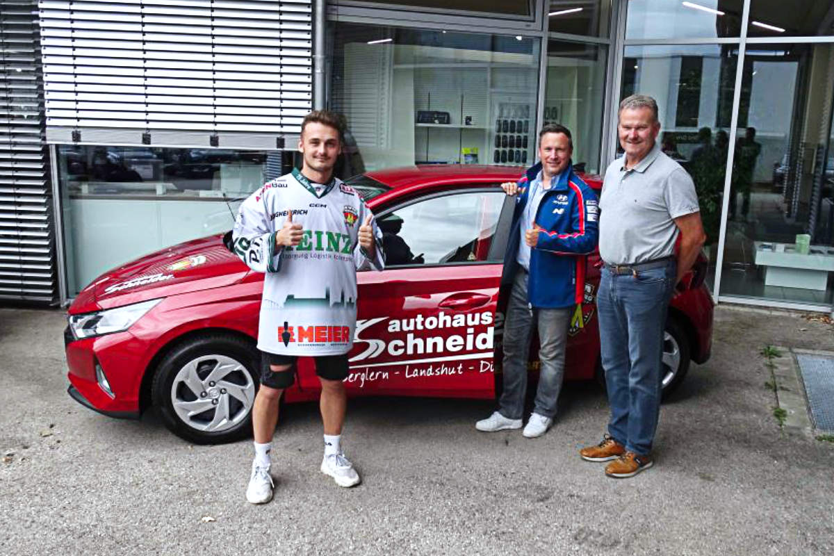Das Autohaus Schneider übergibt einen Hyundai i20 an den EV Moosburg. Drei Männer stehen vor dem roten Auto vor dem Autohaus.
