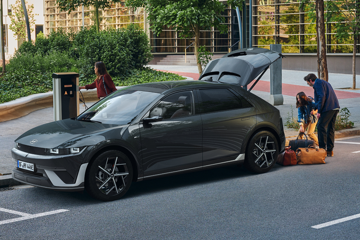Grauer Hyundai IONIQ 5 an einer Ladesäule, während Personen Gepäck aus dem Kofferraum laden.