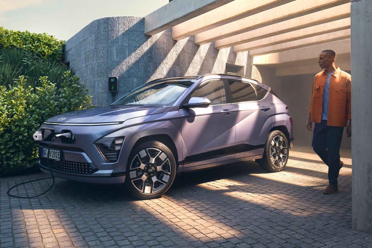 Eine Blaue Hyundai Kona lädt an einer Wallbox vor einem Haus, daneben steht eine Person.