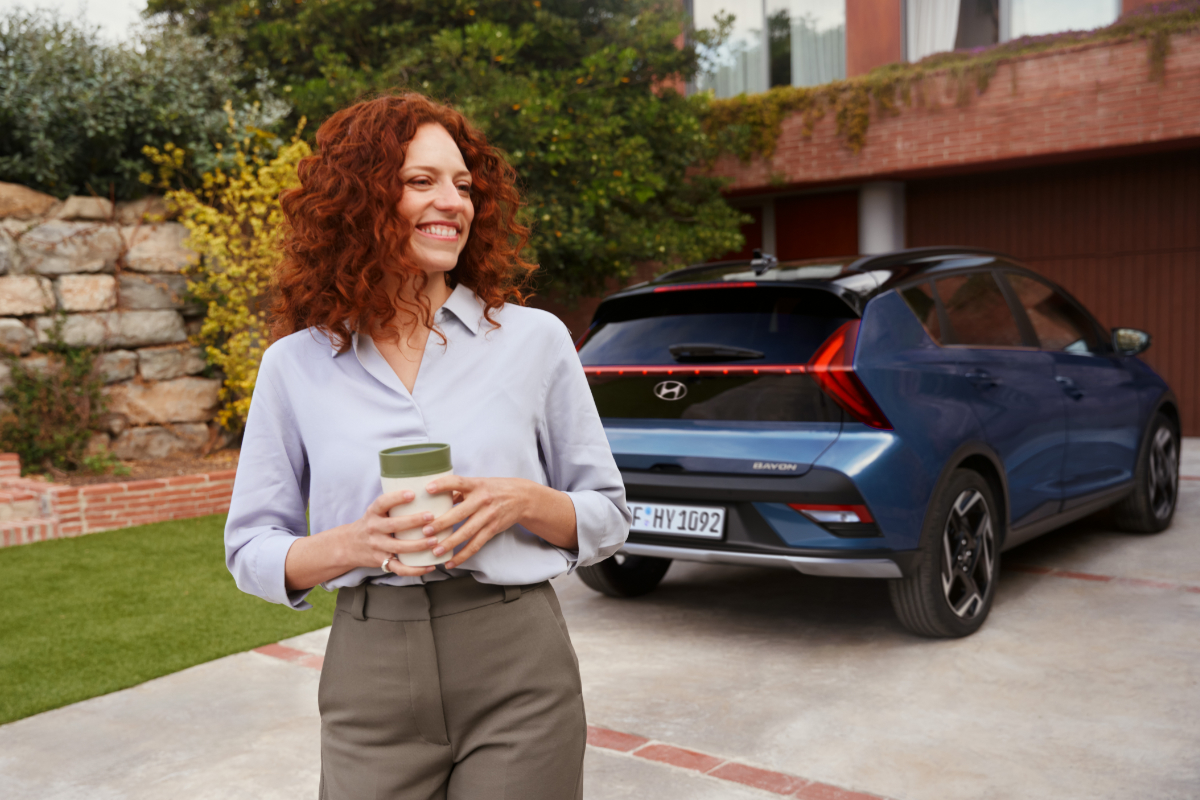 glückliche Frau steht vor einem Blaue Hyundai Bayon