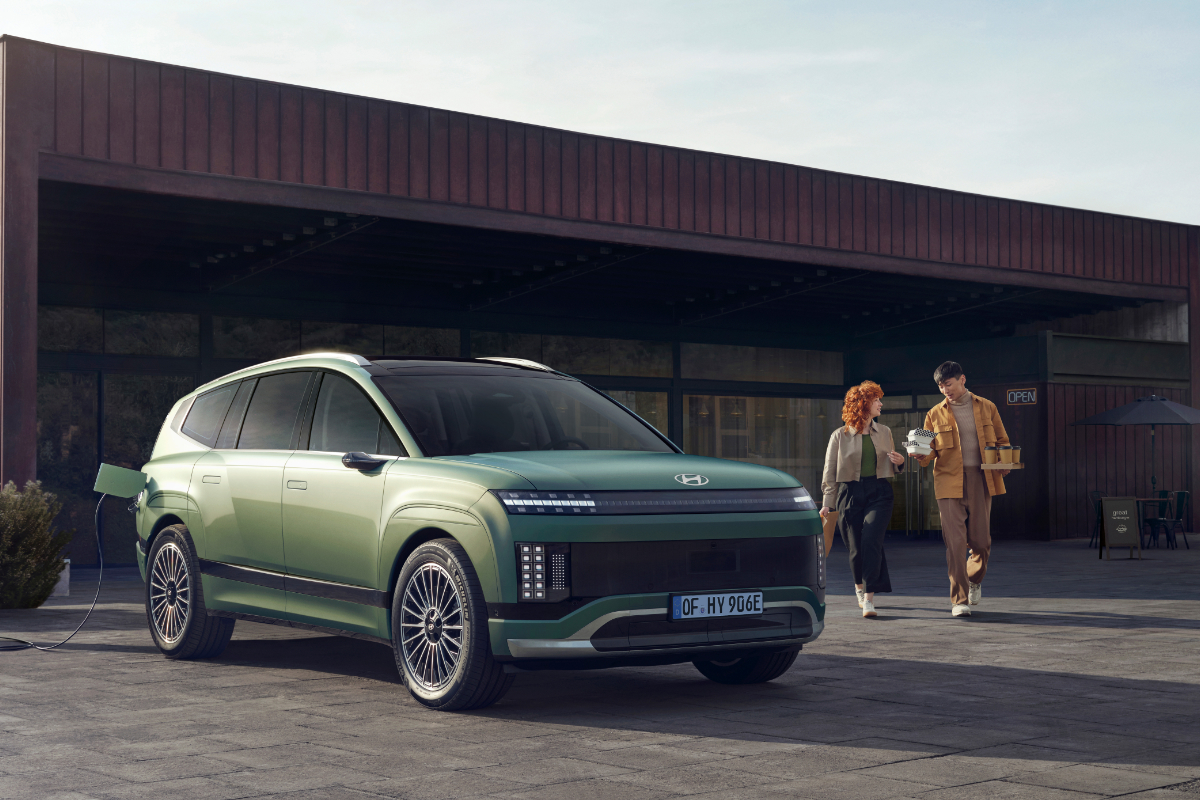 Ein Hyundai IONIQ 9 steht vor einem Café. Ein Mann und eine Frau halten Kaffee in der Hand und gehen auf das Auto zu