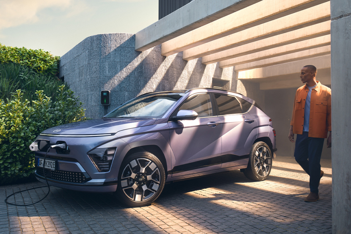 Person lädt Hyundai KONA Elektro an einer Ladestation vor einem modernen Gebäude.
