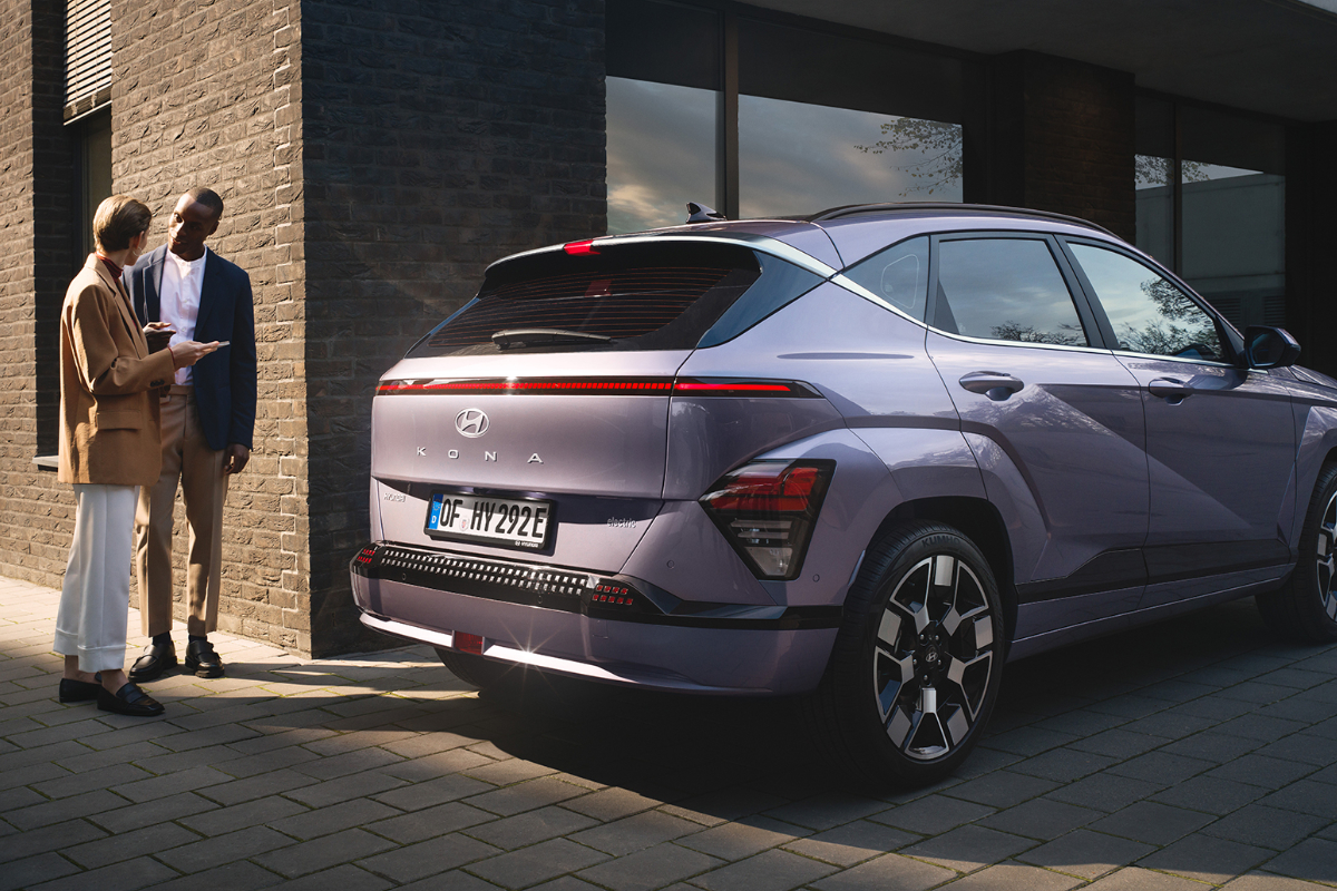 Ein lilafarbener Hyundai KONA Elektro steht vor Geböude. Zwei Personen stehen neben ihm und reden mit einander