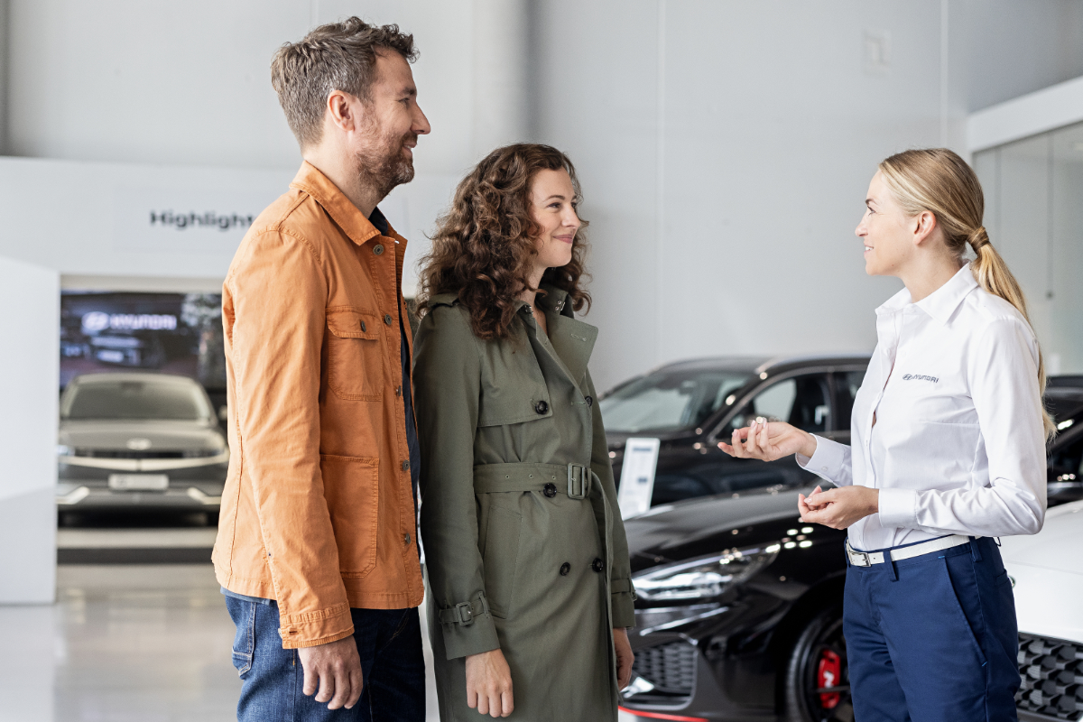 Eine Verkaufsberaterin spricht mit einem Kundenpaar im Autohaus