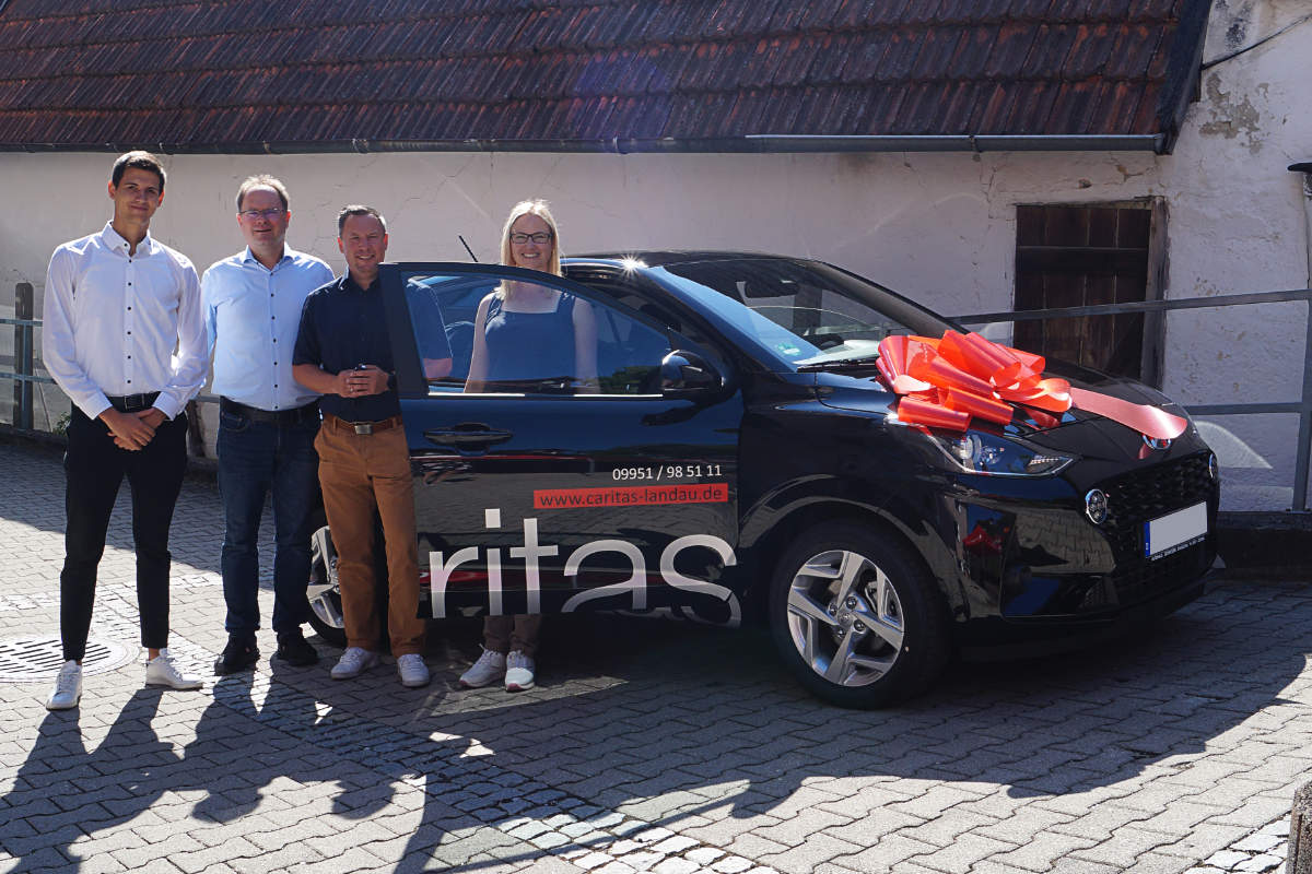 Mitarbeiter des Autohauses Schneider und der Caritas Landau stehen neben dem Auto
